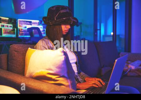 Woman, hacker and programmer typing on laptop in home at night in neon to hack software. Cybersecurity sofa, ransomware phishing and female coder Stock Photo