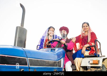 Happy punjabi sikh farmer family driving tractor at agriculture field outdoor. Stock Photo