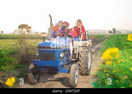 Happy punjabi sikh farmer family driving tractor at agriculture field outdoor. Rural india. Stock Photo