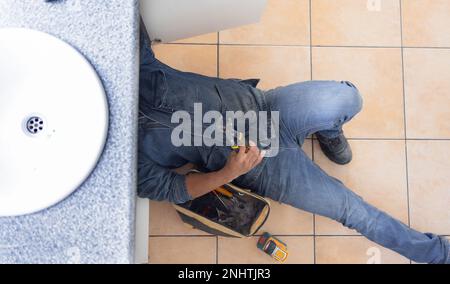 Top view, plumbing and man on floor of maintenance service, engineering or renovation in house. Above of handyman, plumber and contractor with Stock Photo