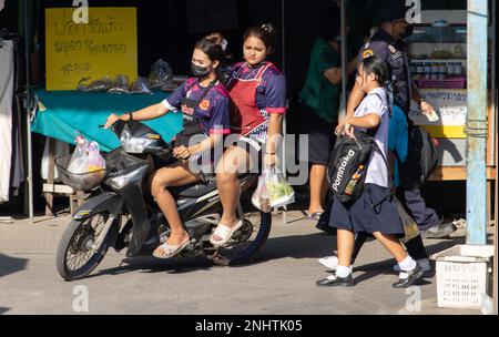 SAMUT PRAKAN, THAILAND, FEB 13 2023, Two women in aprons ride through the marketplace on a motorcycle Stock Photo
