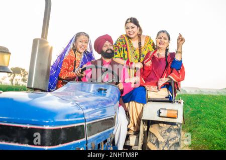 Happy punjabi sikh farmer family sitting on tractor dancing and celebrating outdoor. punjab and haryana people, Rural india. Stock Photo