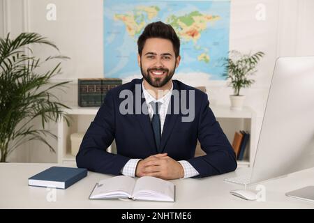 Happy manager with notebook sitting at desk in travel agency Stock Photo