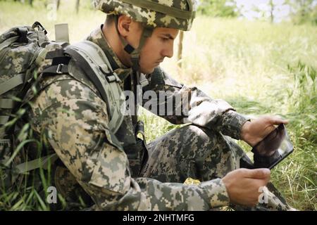 Soldier with backpack using tablet in forest Stock Photo