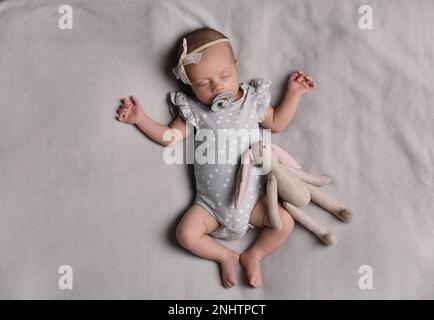 Adorable newborn baby with pacifier and toy bunny sleeping on bed, top view Stock Photo
