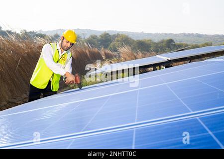 Young indian worker technician installing heavy solar panels outdoors. Exterior solar system installation, alternative renewable green energy generati Stock Photo