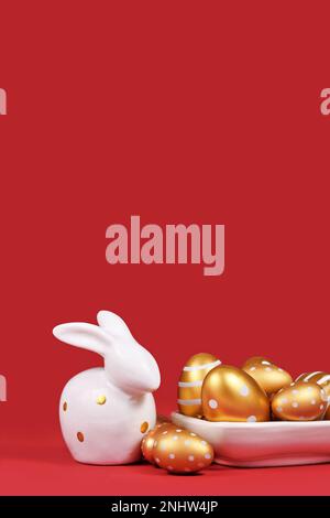 Golden Easter eggs painted with stripes and dots and bunny on red background with copy space Stock Photo