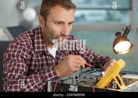 man repairing a computer using a multimeter Stock Photo