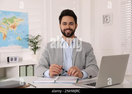 Happy manager with notebook sitting at desk in travel agency Stock Photo