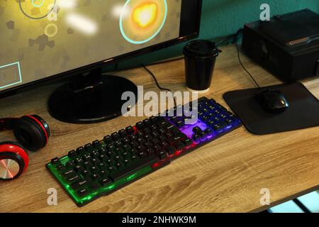 Modern RGB keyboard, computer and headphones on wooden table indoors Stock Photo