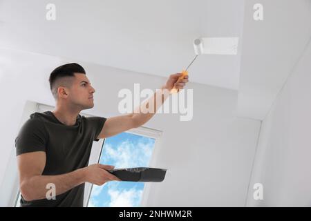 Man painting ceiling with roller in room Stock Photo