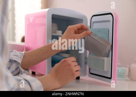 Woman taking cosmetic product from mini fridge indoors, closeup Stock Photo