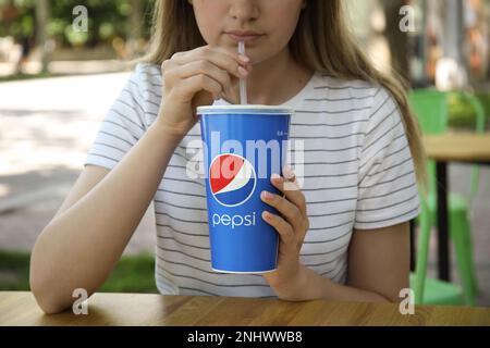 MYKOLAIV, UKRAINE - JUNE 9, 2021: Woman drinking Pepsi from paper cup at table in outdoor cafe, closeup Stock Photo