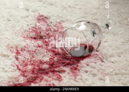 Overturned glass and spilled red wine on white carpet Stock Photo
