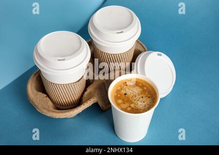 Takeaway paper coffee cups with sleeves, plastic lids and cardboard holder on blue background Stock Photo