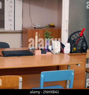 Teacher's desk with a laptop and a stack of papers in the classroom in front of the blackboard Stock Photo
