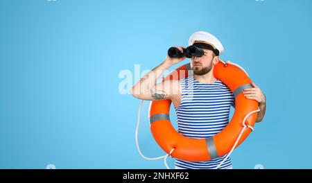 Sailor with binoculars and ring buoy on light blue background Stock Photo