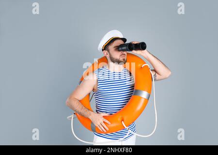 Sailor with binoculars and ring buoy on light grey background Stock Photo