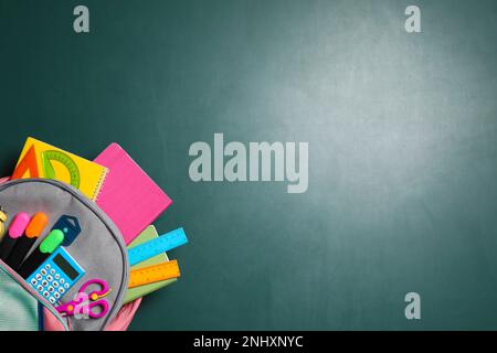 Backpack with different stationery on chalkboard background, top view. Space for text Stock Photo