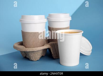 Takeaway paper coffee cups with sleeves, plastic lids and cardboard holder on blue background Stock Photo