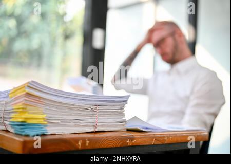 Pile of unfinished document paperwork or a stack of financial report on the table over blurred background of stressed businessman sits at the table. c Stock Photo