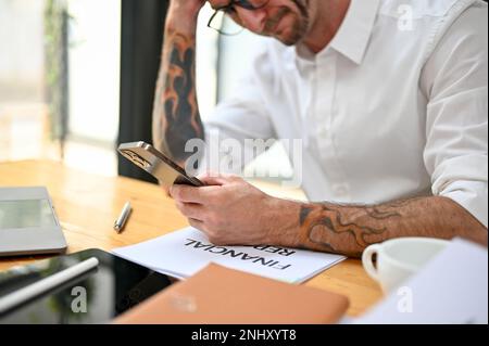 Stressed and frustrated Caucasian businessman or business entrepreneur using his phone at his desk, receiving bad news on the message, having a busine Stock Photo