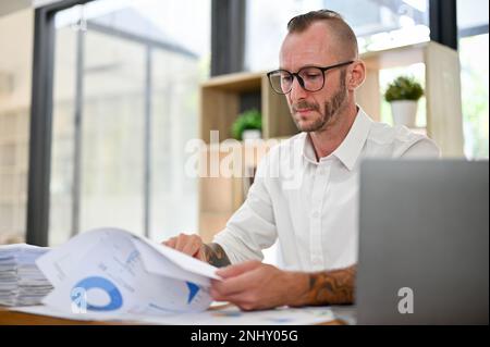 Focused and professional Caucasian businessman or male financial consultant analyzing, examining and working on financial data report at his desk in t Stock Photo