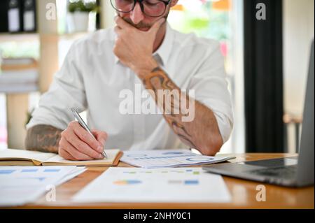 Cropped image of a thoughtful and focused Caucasian businessman working on financial data report, analyzing his business financial potential, noting s Stock Photo