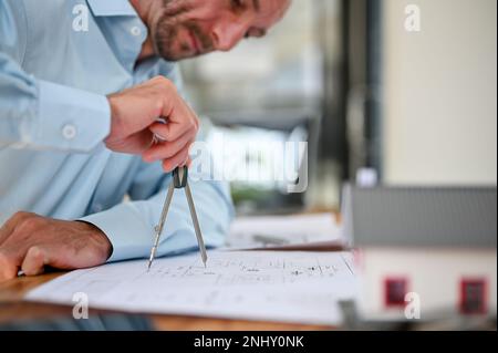 Professional and smart Caucasian male engineer or architect using a divider compass, drawing and checking scale on a blueprint, working in the office. Stock Photo