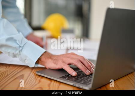 Close-up image of a professional Caucasian male engineer or contractor using laptop, typing on keyboard, working in the office. Stock Photo