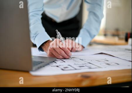 Close-up image of a professional male engineer checking scale and building plan design on a blueprint, holding pen, working at his desk in the office. Stock Photo