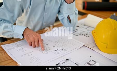 Close-up image of a professional male engineer or contractor man checking a blueprint, looking at the building plan, finger pointing on a blueprint, w Stock Photo