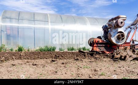 A farmer drives a small tractor, walking behind the tractor, plowing the land. Work on the field. The concept of agriculture and industry. High quality photo Stock Photo