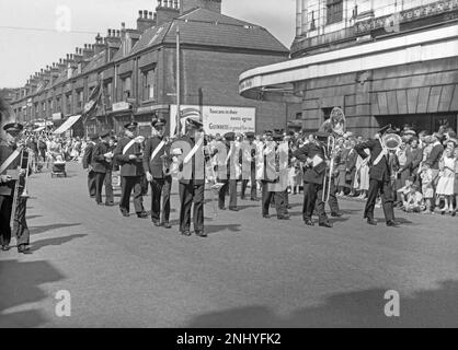 A Whit Walks procession in Union Street, Oldham, Greater Manchester, Lancashire, England, UK c.1960. The Salvation Army brass band is in the foreground. The Church of England religious event traditionally took place on Whit Friday, with children heavily involved along with brass and silver bands. First held in Manchester over 200 years ago in 1801, these were held to encourage community activity over the Whit holiday break. Whit Walks in Manchester now takes place on the Spring Bank Holiday Monday. This is taken from an old black and white negative – a vintage 1950s/60s photograph. Stock Photo