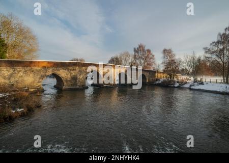 Twyford Bridge the River Medway at Yalding covered in snow as setting sunshine dapples light on stonework peaceful deep dark water downstream of weir Stock Photo
