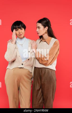 worried asian woman looking at middle aged mother having headache isolated on coral background Stock Photo
