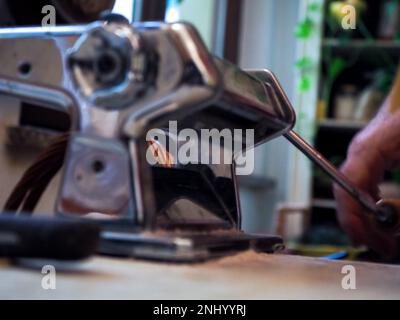 caucasian senior man hand rolling dough for homemade uncooked pasta from italian machine maker in hands with semolina flour over white marble texture Stock Photo