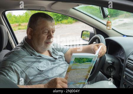 Portrait of Ukainian senior SittiCang sitting inside his car and reading book Stock Photo