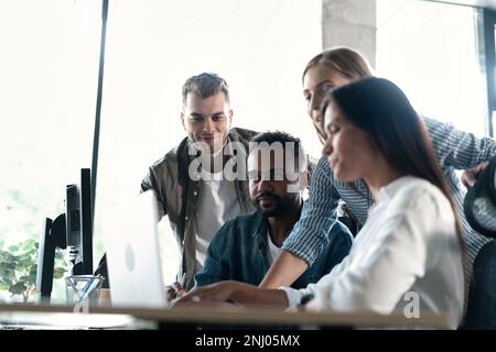 Friendly creative diverse colleagues team discuss online project use computer at workplace Stock Photo