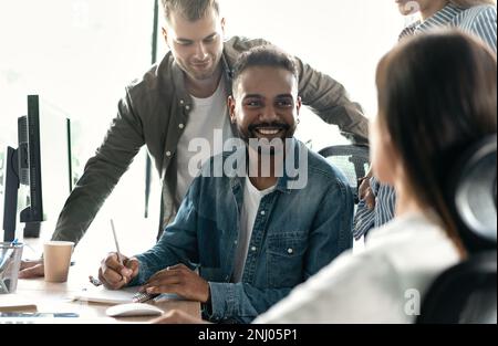Friendly creative diverse colleagues team discuss online project use computer at workplace Stock Photo