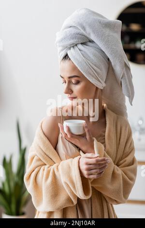 Young woman in towel on head and bathrobe holding cosmetic cream,stock image Stock Photo