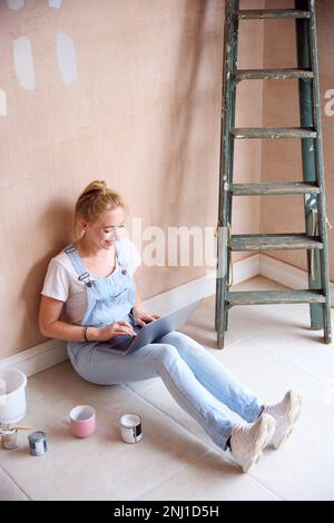 Woman Renovating Kitchen At Home Sits On Floor With Laptop Taking A Break From Decorating Kitchen Stock Photo