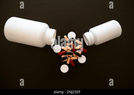 Two white jars with scattered red, pink and black medicines on a dark table. Stock Photo