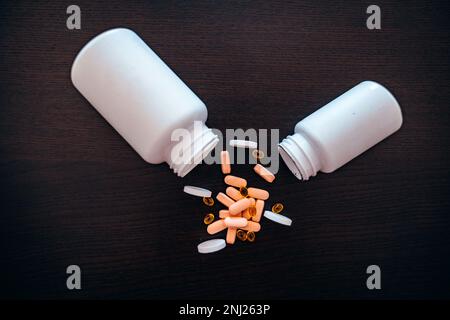 Two white jars with scattered red, pink and black medicines on a dark table. Stock Photo