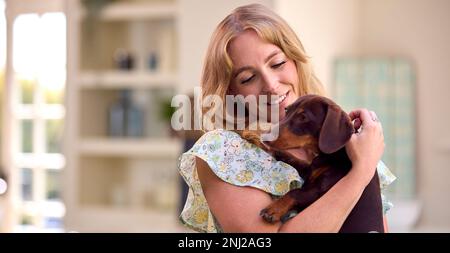 Woman At Home Holding And Stroking Pet Dachshund Dog In Kitchen Stock Photo