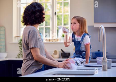 Family With Daughter Helping Older Mother To Do Washing Up In Kitchen At Home Blowing Soap Bubbles Stock Photo
