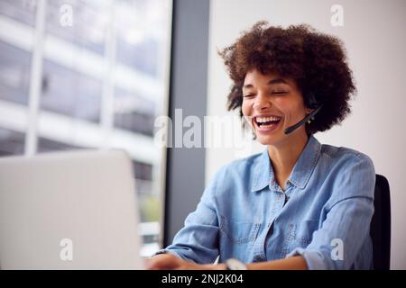 Young Businesswoman In Modern Office Working On Laptop Using Wireless Headset Stock Photo