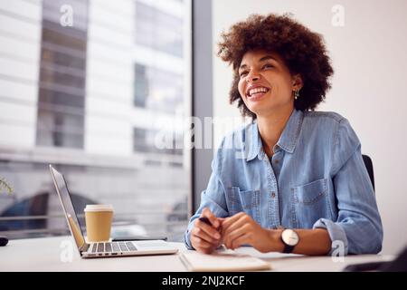 Young Businesswoman In Modern Office Working On Laptop Making Notes In Notebook Stock Photo