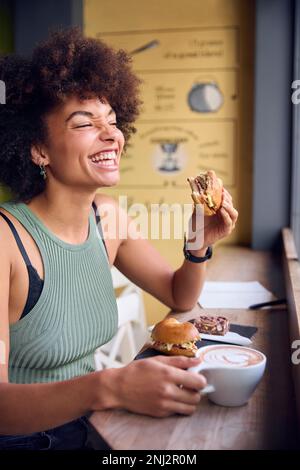 Female Customer In Coffee Shop Window Eating Bagel Sandwich For Lunch Stock Photo