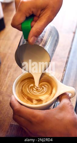 Close Up Of Barista Pouring Steamed Milk Into Cup Of Coffee In Cafe Making Foam Art Decoration Stock Photo